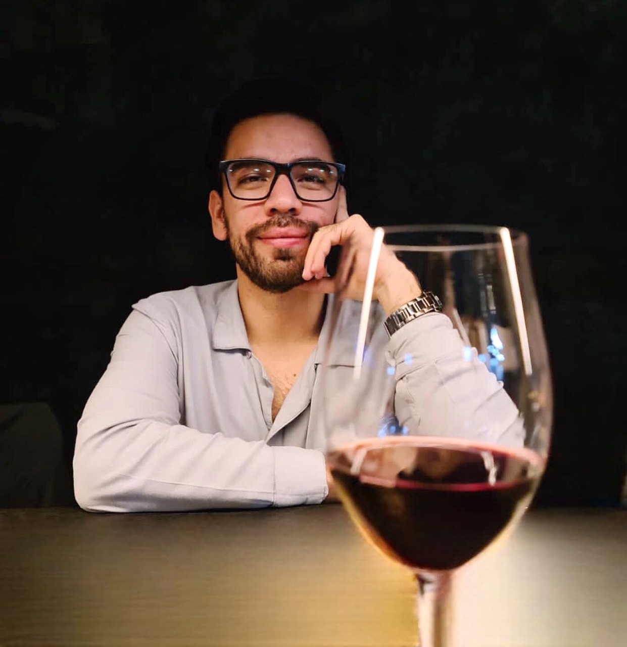 José Sainz sentado, con una copa de vino en primer plano y fondo oscuro